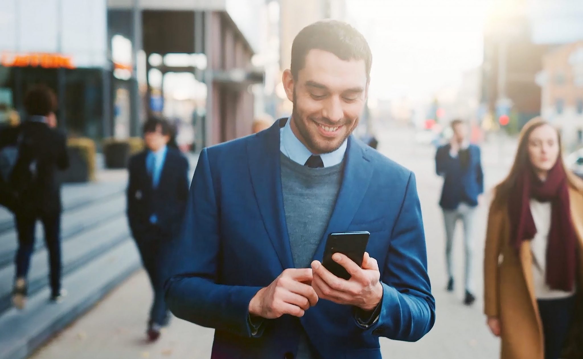 Auf einer belebten Straße sieht ein Mann auf sein Telefon und lächelt.