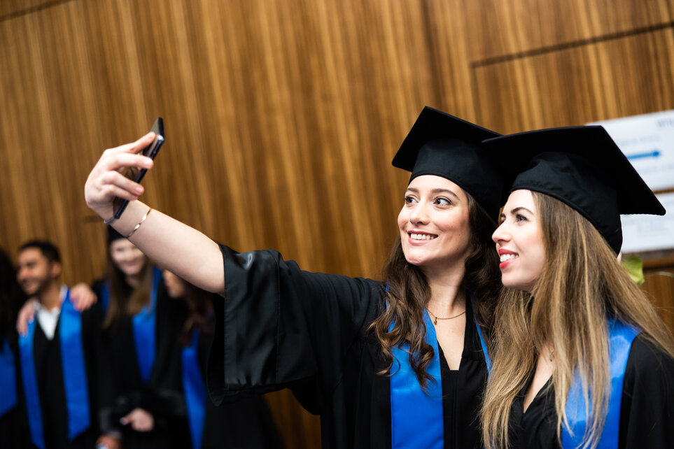 Zwei Studierende, die ihren Abschluss feiern und ein Selfie machen